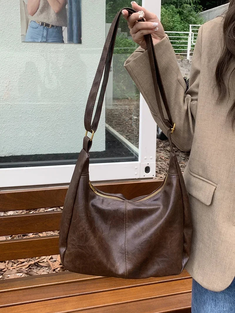 A brown vintage PU leather tote bag with a crossbody strap is displayed on a wooden surface.