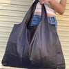 شخص يحمل حقيبة تسوق سوداء كبيرة قابلة للطي على حائط فاتح اللون.