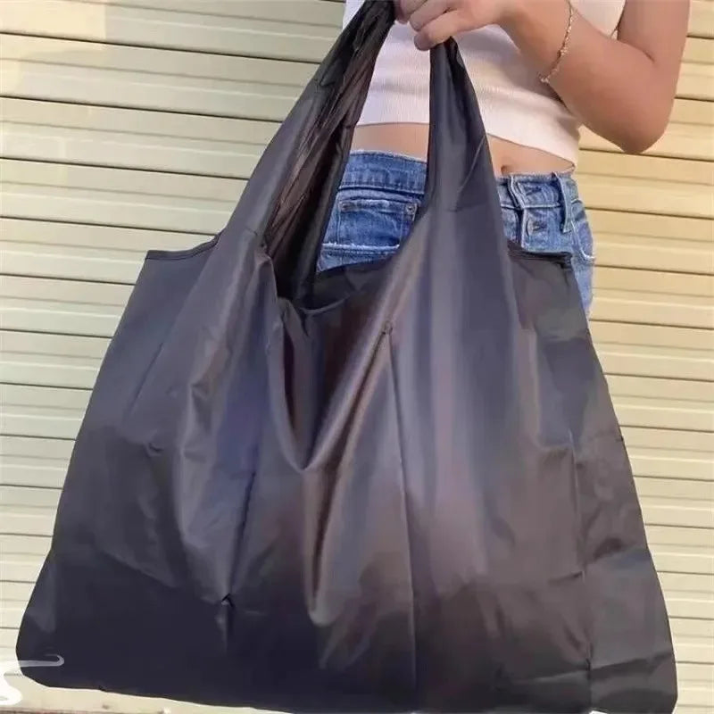 شخص يحمل حقيبة تسوق سوداء كبيرة قابلة للطي على حائط فاتح اللون.