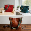 A geometric strap crossbody hobo bag in deep red leather with gold accents, shown next to a white cup and a green suede bag.
