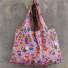 A pink reusable shopping bag with a colorful pattern featuring cartoon animals and faces.