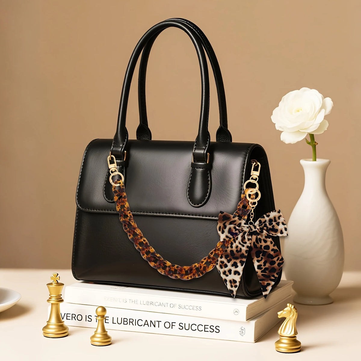 Schwarze Acrylhandtasche mit Leopardenmuster-Kette und Schleifchen-Anhänger auf einem Stapel Bücher.