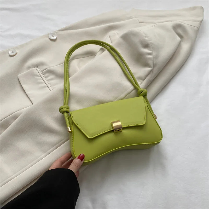 A lime green leather crossbody bag with a gold clasp is being held against a light beige blazer.