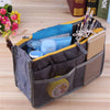 A gray multi-pocket organizer tote bag filled with makeup brushes, cosmetics, and other essentials on a wooden surface.