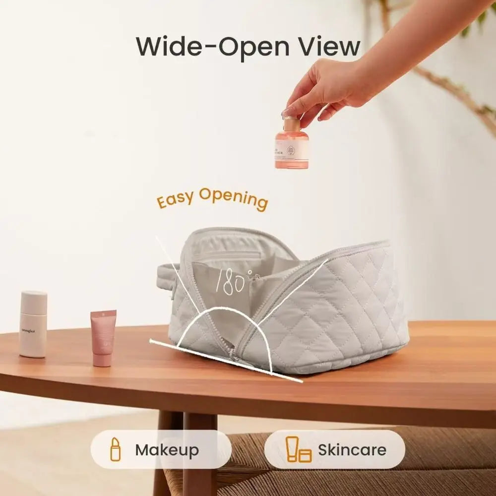 A hand is opening a lay-flat water-resistant makeup organizer bag, showing its easy opening feature on a wooden table.