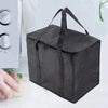 A dark gray foldable insulated grocery and food cooler bag is shown next to a hand and a white appliance.