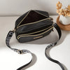 Black quilted crossbody camera bag with a gold letter strap resting on a white surface.