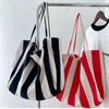 Three striped canvas tote bags in black white and red hanging on a metal rack.