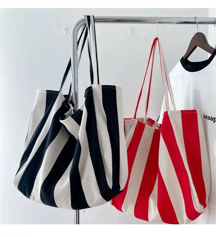 Three striped canvas tote bags in black white and red hanging on a metal rack.