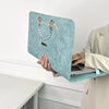 A light blue suede laptop sleeve with gold hardware is held by a person in a light jacket.