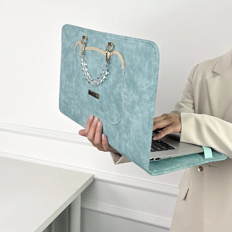 A light blue suede laptop sleeve with gold hardware is held by a person in a light jacket.