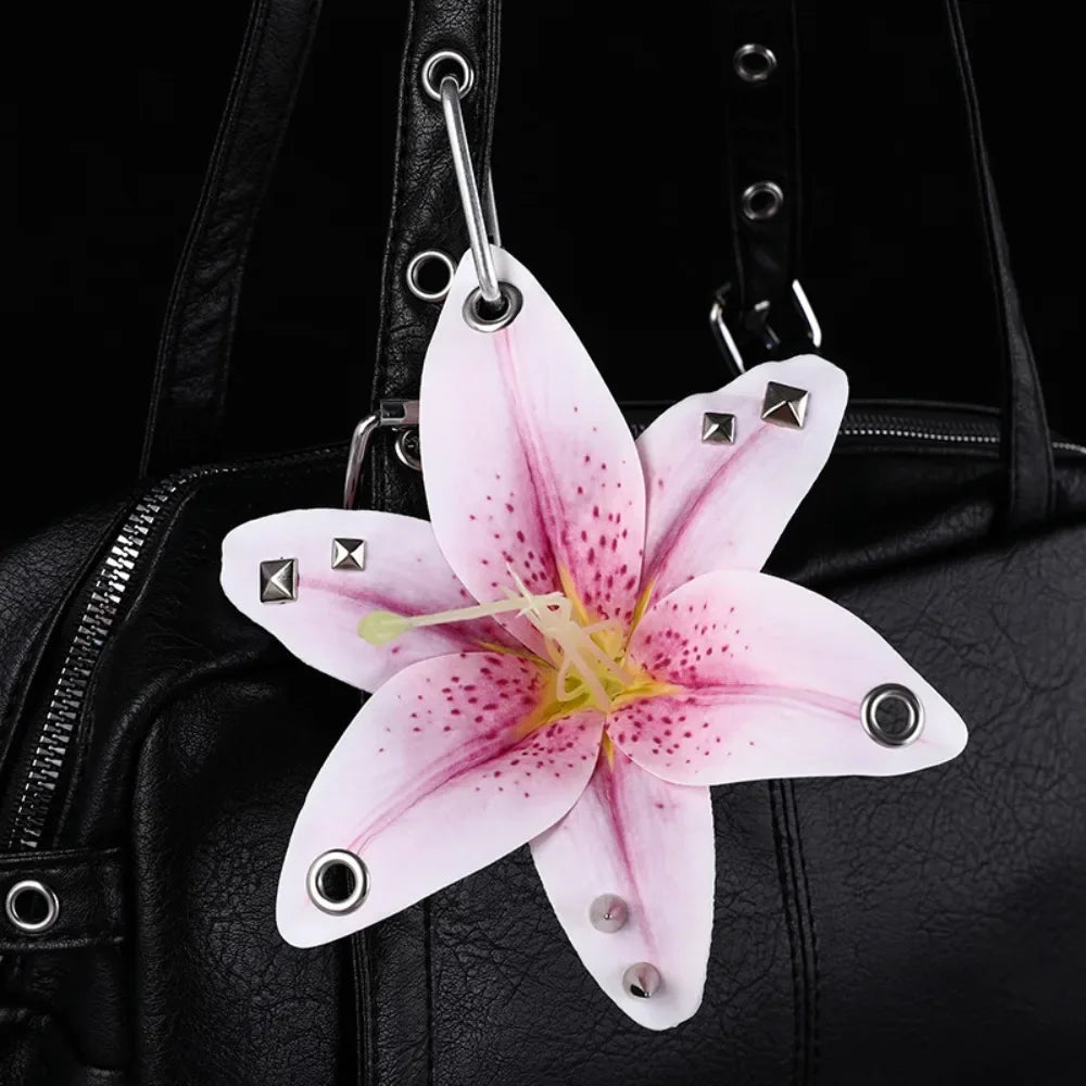 A pink orchid flower keychain with magenta spots is attached to a black leather handbag.