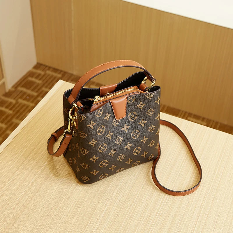 A brown leather bucket bag with a gold zipper and adjustable strap rests on a light wooden surface.