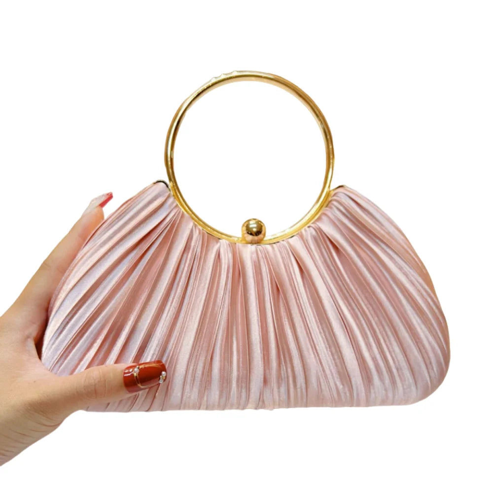 A hand holds a pink satin pleated evening clutch bag with a gold rim.