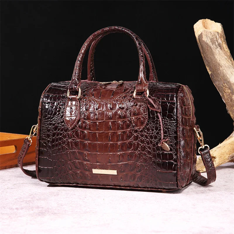 A dark brown crocodile pattern leather crossbody tote bag resting on a light surface next to a piece of wood.