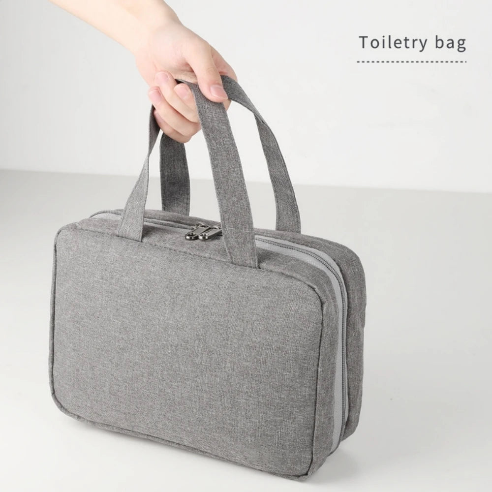 A gray toiletry bag with fabric handles is being held by a hand, shown against a white background.