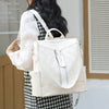 A woman is carrying a cream-colored leather anti-theft backpack with silver zippers and a white striped shirt.