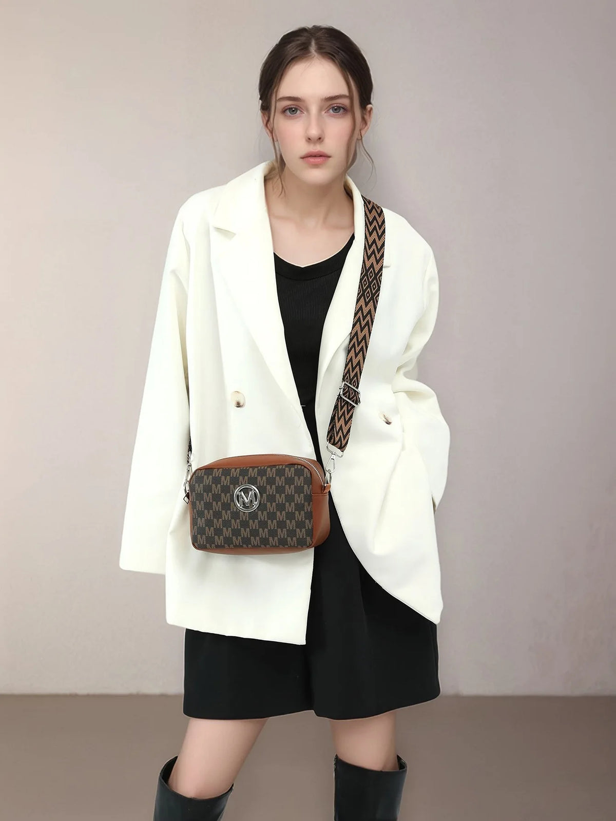 A woman models a white blazer and black outfit with a brown patterned crossbody bag.