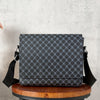 A dark gray patterned flap crossbody bag resting on a wooden stool against a light gray background.