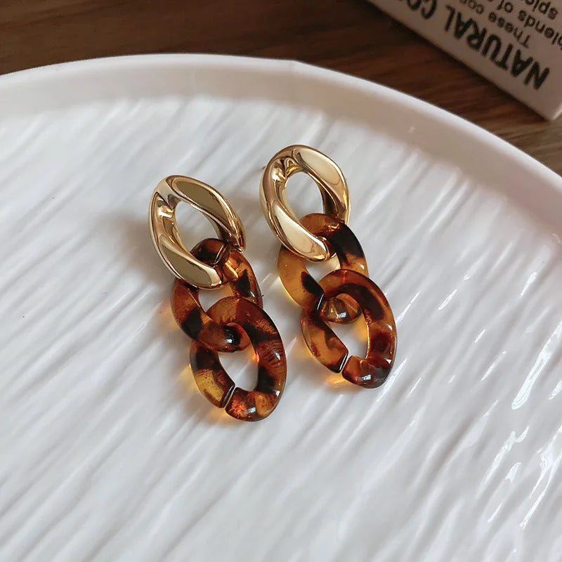 A pair of gold-toned interlocking dangle earrings featuring a leopard print finish, displayed on a white plate.