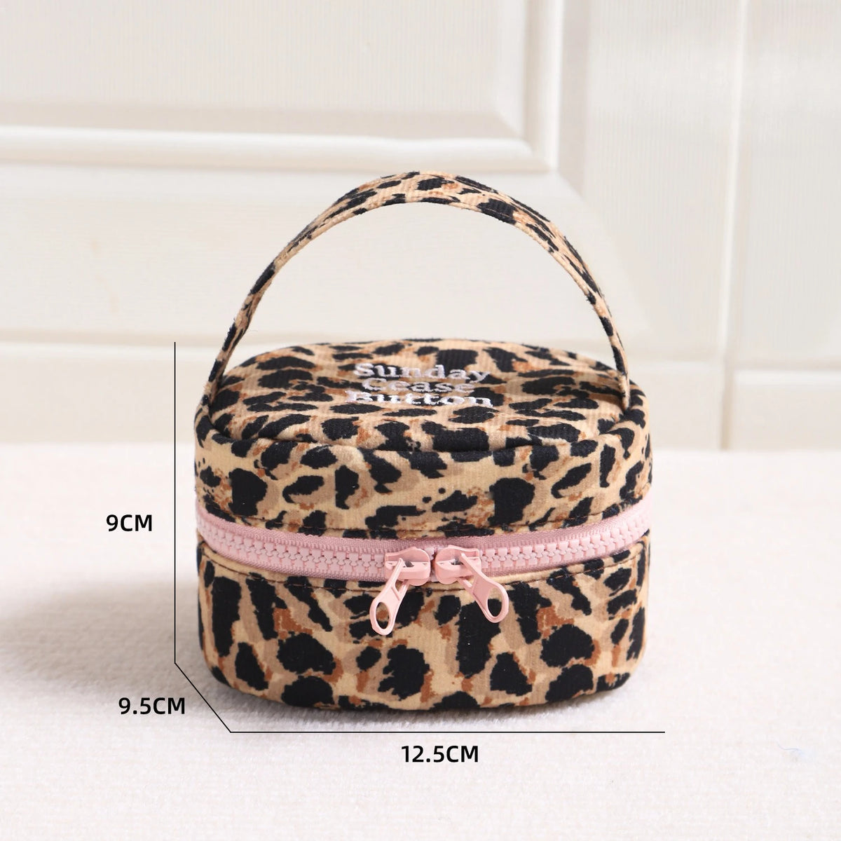 Bolsa de maquillaje redonda con estampado de leopardo y cremallera rosa, mostrada sobre fondo blanco.