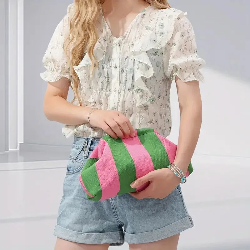 Una mujer modela un bolso de mimbre rayado rosa y verde con una blusa floral blanca y pantalones cortos de mezclilla.