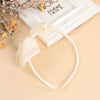 A set of twenty solid color bow hairbands for girls displayed next to a white frame and floral branches.