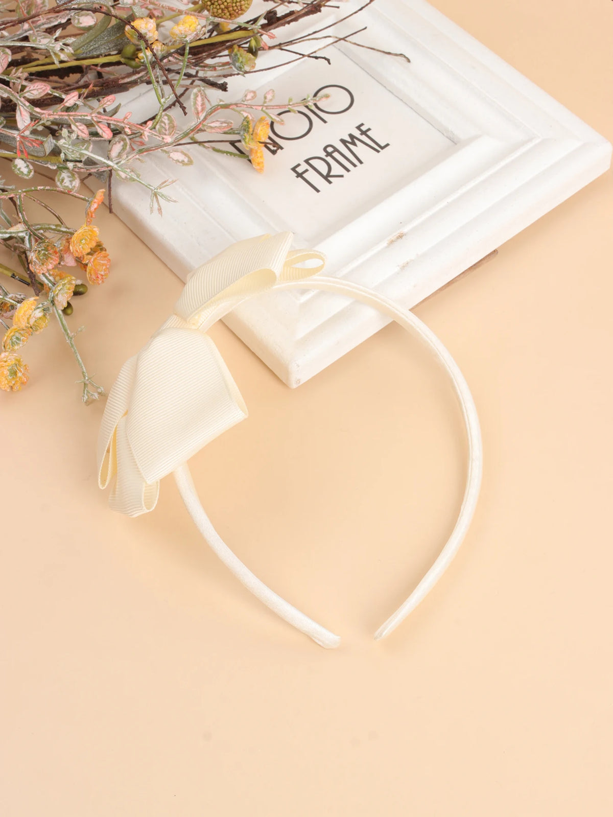A set of twenty solid color bow hairbands for girls displayed next to a white frame and floral branches.