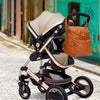 A beige and brown large capacity diaper bag backpack is shown on a cobblestone street.