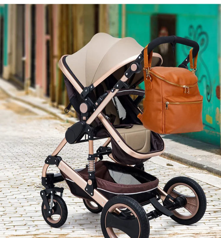 A beige and brown large capacity diaper bag backpack is shown on a cobblestone street.