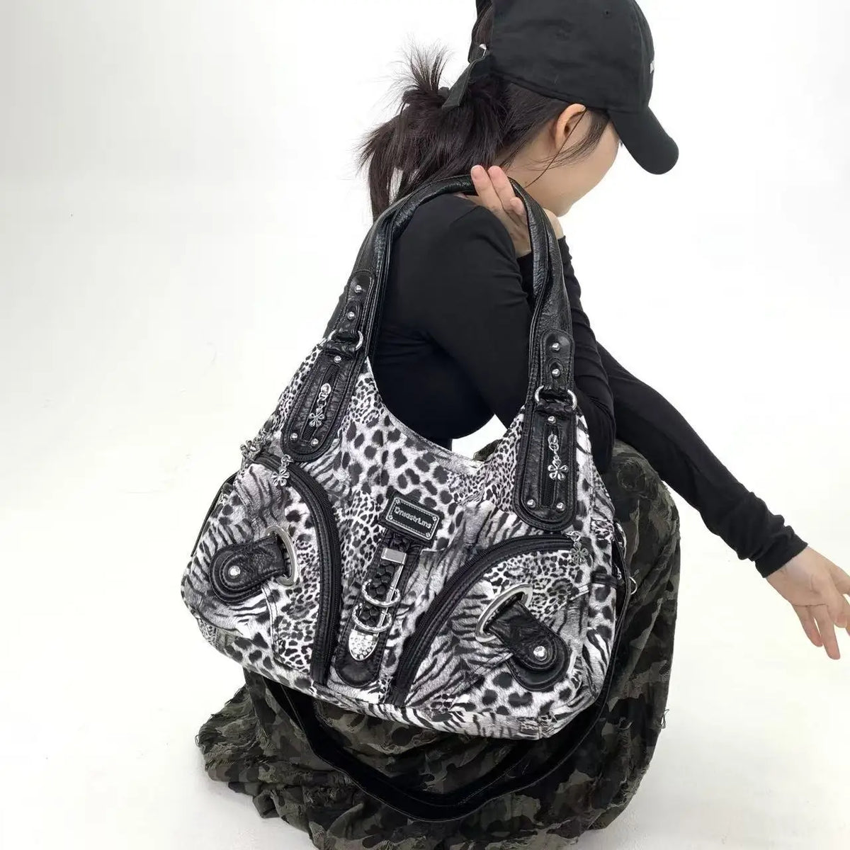 A woman wearing a black hat and black top holds a leopard print crossbody shoulder bag with multiple compartments.
