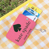 A pink card holder with a spade design and the name Kate Spade is shown next to a yellow plaid cloth and a stack of credit ca