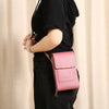 A person wearing a black top and pants holds a pink RFID-protected touch screen crossbody bag.