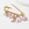 Gold-toned alloy brooch pin featuring a pearl, pink bow, and a pink leather handbag charm.
