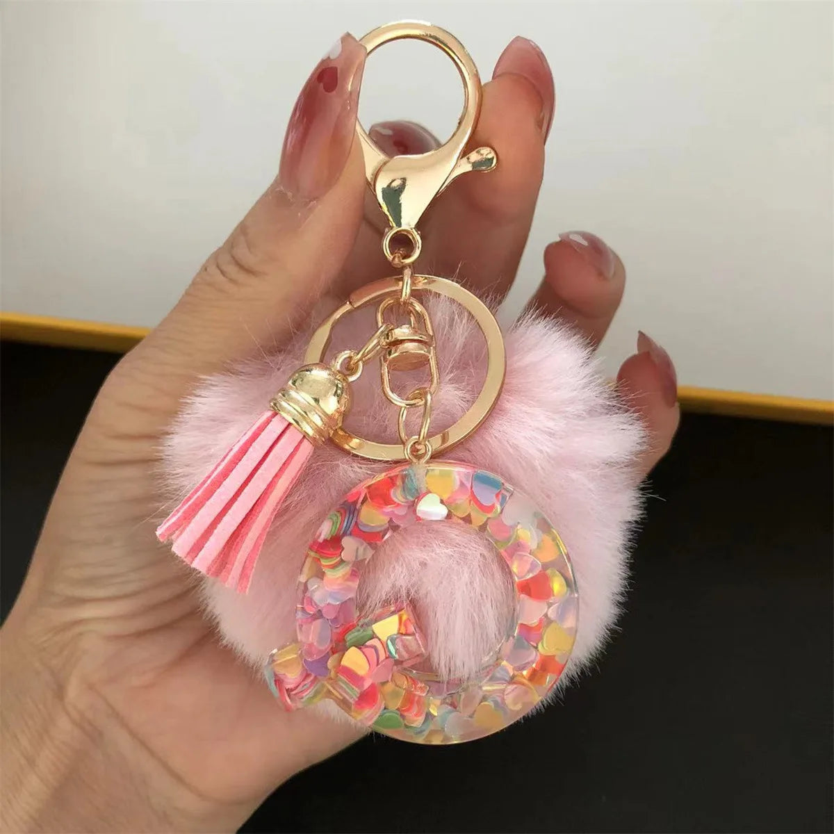 A hand holds a custom initial letter keychain featuring a shiny resin pendant and pink alphabet charm.