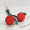 A red cherry fruit shape coin purse keychain with green leather strap resting on a white marble surface.