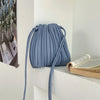 A light blue PU leather pleated crossbody bag hanging on a white shelf next to a stack of books.