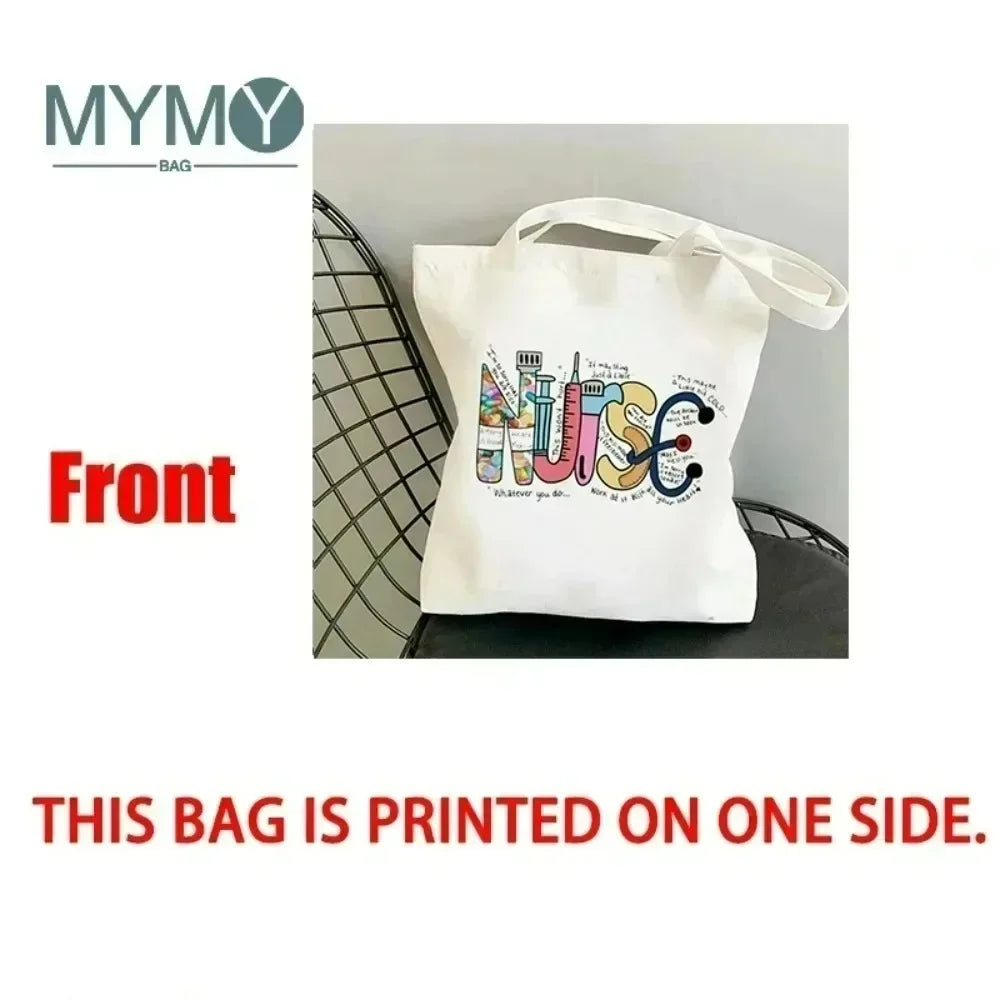 A white canvas tote bag with an alphabet and floral print is shown against a gray background.