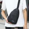 A black men's versatile crossbody sling chest bag is being held by a person wearing a white t-shirt.