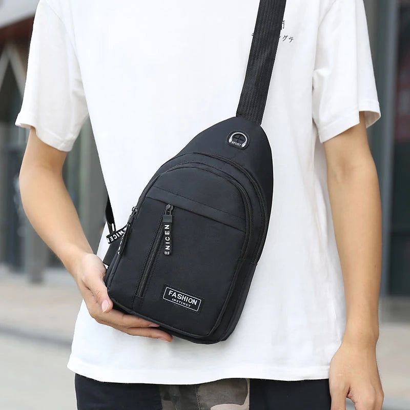 A black men's versatile crossbody sling chest bag is being held by a person wearing a white t-shirt.