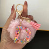 A hand holds a custom initial letter keychain featuring a shiny resin pendant and pink alphabet charm.