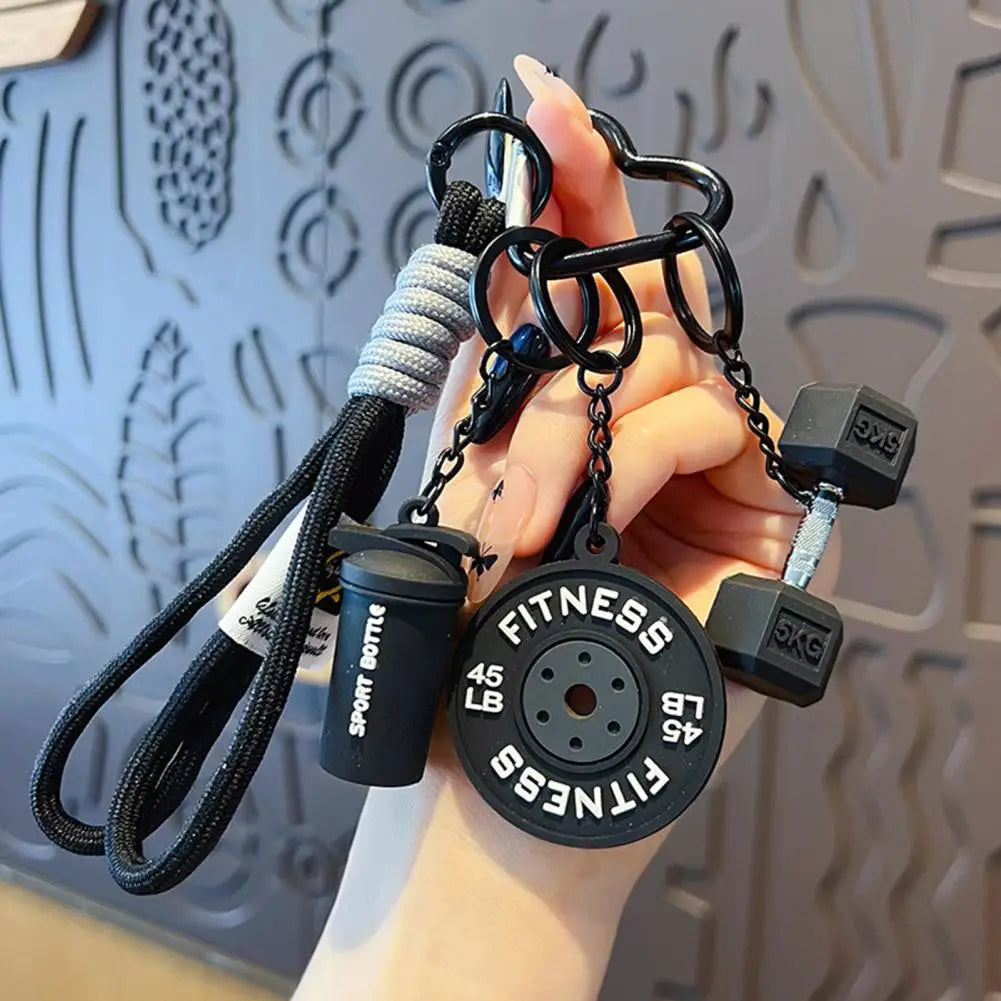 A hand holds a fitness keychain featuring a dumbbell and kettlebell charm.