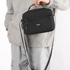 A hand holds a black compact waterproof crossbody messenger bag against a light gray jacket.