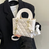 A cream quilted handbag with gold chain accents is held by a person wearing a black blazer.