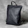 A black genuine full-grain leather backpack is shown against a gray background.