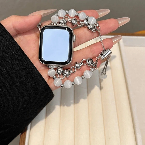 A hand holds an adjustable metal link bracelet with crystal beads and a square smartwatch.