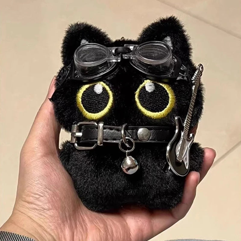 Colgante de llavero de un peluche de gato negro con grandes ojos amarillos y una hebilla plateada, sostenido en una mano.