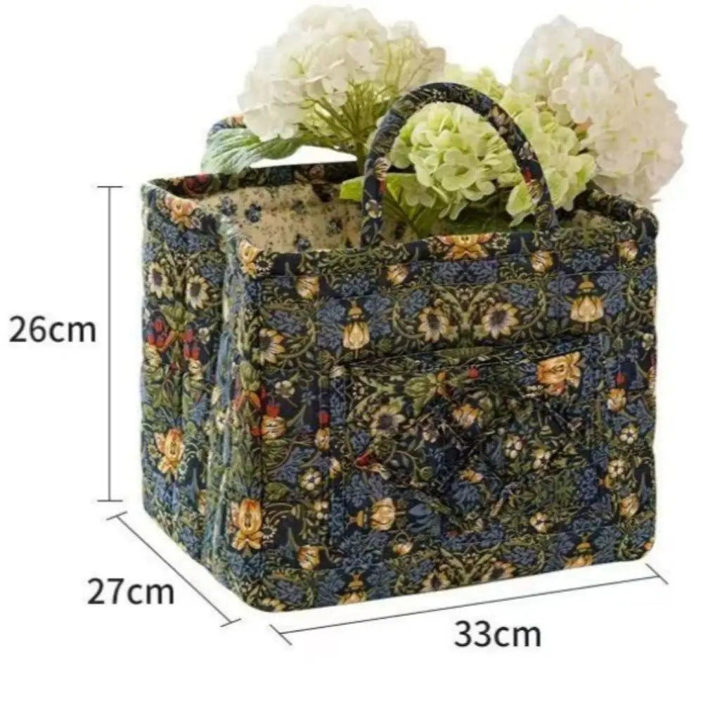 A quilted fabric storage basket with carry handles featuring a dark green and blue floral pattern.