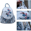 A light gray linen backpack featuring delicate floral embroidery details.