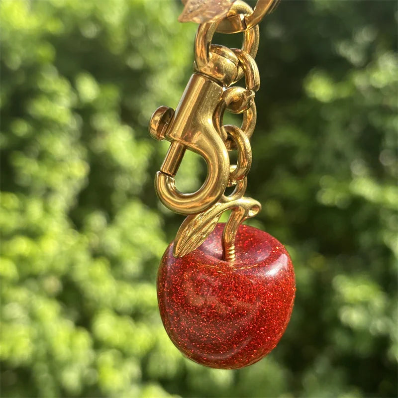A gold-colored crystal fruit charm keychain hanging against a blurred green background.